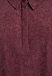 Burgundijas ribota polo krekls ar apkakli un pogu, kas piestiprināta pie apkakles. Audums izskatās mīksts un teksturēts.