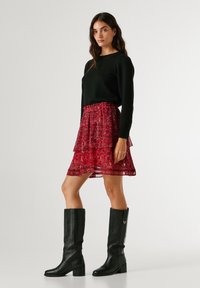 Musta struktuuriga sviiter, kihiline punane lilleline seeliku ja põlvekõrgused mustad nahast saapad, millel on jäme konts ja dekoratiivne riistvara.