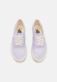Baskets en toile lilas avec lacets blancs et semelles en caoutchouc. Présente un orteil arrondi et un design minimaliste. Logo Vans visible sur la semelle intérieure.