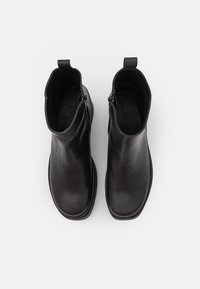 Bottines en cuir noir avec une finition lisse, bout arrondi et fermeture éclair sur le côté. Semelle en caoutchouc plate avec un branding discret à l'intérieur.