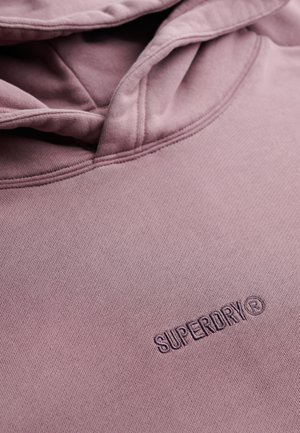 Sudadera con capucha rosa hecha de tela suave con una superficie texturizada; presenta un logo "SUPERDRY" cosido en el frente. Diseño clásico con capucha.