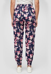 Blomsterdekte joggesbukser i marineblått med rosa og hvite blomster. Elastisk midjebånd og mansjetter. Kombinert med hvite sneakers.