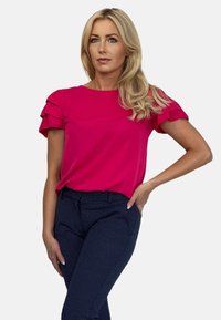 Fuksjowa bluzka z falbaniastymi rękawami, połączona z granatowymi spodniami w kropki. Gładki materiał, luźny krój i subtelne detale przeszycia.