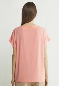 Lys pink kortærmet top lavet af blød, let stof med en afslappet pasform og en bred halsudskæring. Glat tekstur uden synlige mønstre.