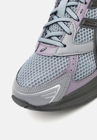  Lichtblauw mesh hardloopschoen met grijze en lila accenten, met een gestructureerd oppervlak en reflecterend materiaal aan de zijkant en op de neus.