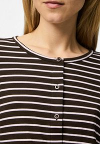 Brun och vit randig topp med rund halsringning, med en knappslå fram och en mjuk stickad struktur.