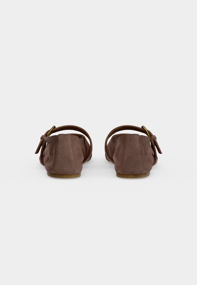 Paire de chaussures plates en daim marron avec brides à la cheville et boucles dorées, vues de dos sur un fond clair uni.