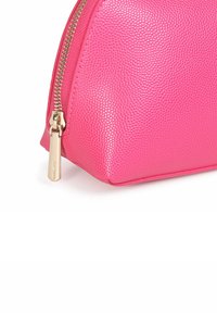 Borsa cosmetica rosa testurizzata con cerniera dorata e linguetta, caratterizzata da una forma arrotondata e una finitura liscia. Accentuata da un motivo sottile.