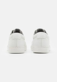 White leather sneakers with a smooth texture, padded gray lining, and a rubber outsole featuring a textured design. Standard lace-up closure.
