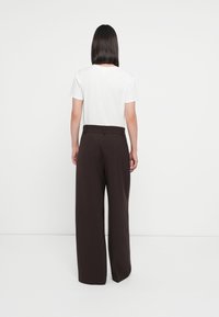 Tricou alb cu mânecă scurtă și pantaloni largi, cu talie înaltă, de culoare maro închis. Pantalonii au o textură netedă și buzunare laterale, fără modele vizibile.