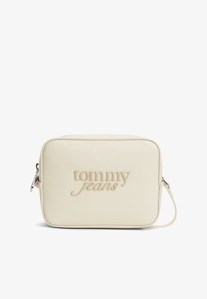 Kreemivärvi ristkere kott reljeefse "tommy jeans" logoga, hõbedaste detailide ja reguleeritava rihmaga valgel taustal.