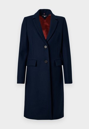 Marineblauer Wollmischmantel mit taillierter Passform, Reverskragen, einreihiger Knopfleiste und zwei siden Taschen. Futter in Burgunderrot.