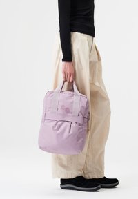 Lila Nylon-Rucksack mit zwei oberen Griffen, einer vorderen Tasche und abgerundeten Ecken. Besitzt zwei pinkfarbene runde Akzente auf der Vorderseite.