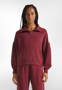 Giacca zip-up bordeaux con ampio colletto, spalle scese e tessuto testurizzato. Presenta tasche frontali e polsini elastici.