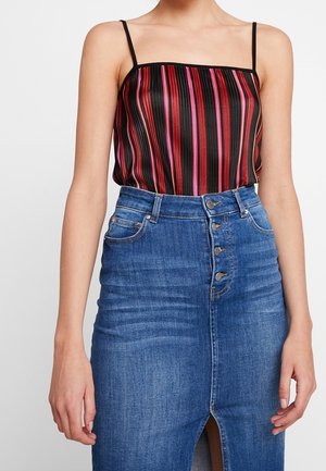 Kobieta ubrana w bezrękawnik w paski z cienkimi czarnymi ramiączkami oraz wysoką, niebieską spódnicę jeansową zapinaną na guziki z przodu i z rozcięciem z przodu.