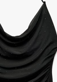 Schwarzes Kleid aus weichem Stoff mit einem drapierten Ausschnitt und funkelnden Strasssteinen, die überall eingearbeitet sind. Ausführliche Raffung auf einer Seite.