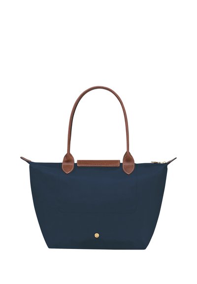 Navy blue tote bag made of fabric with brown leather handles and accent. Features a front pocket and a gold zipper. Simple, spacious design.