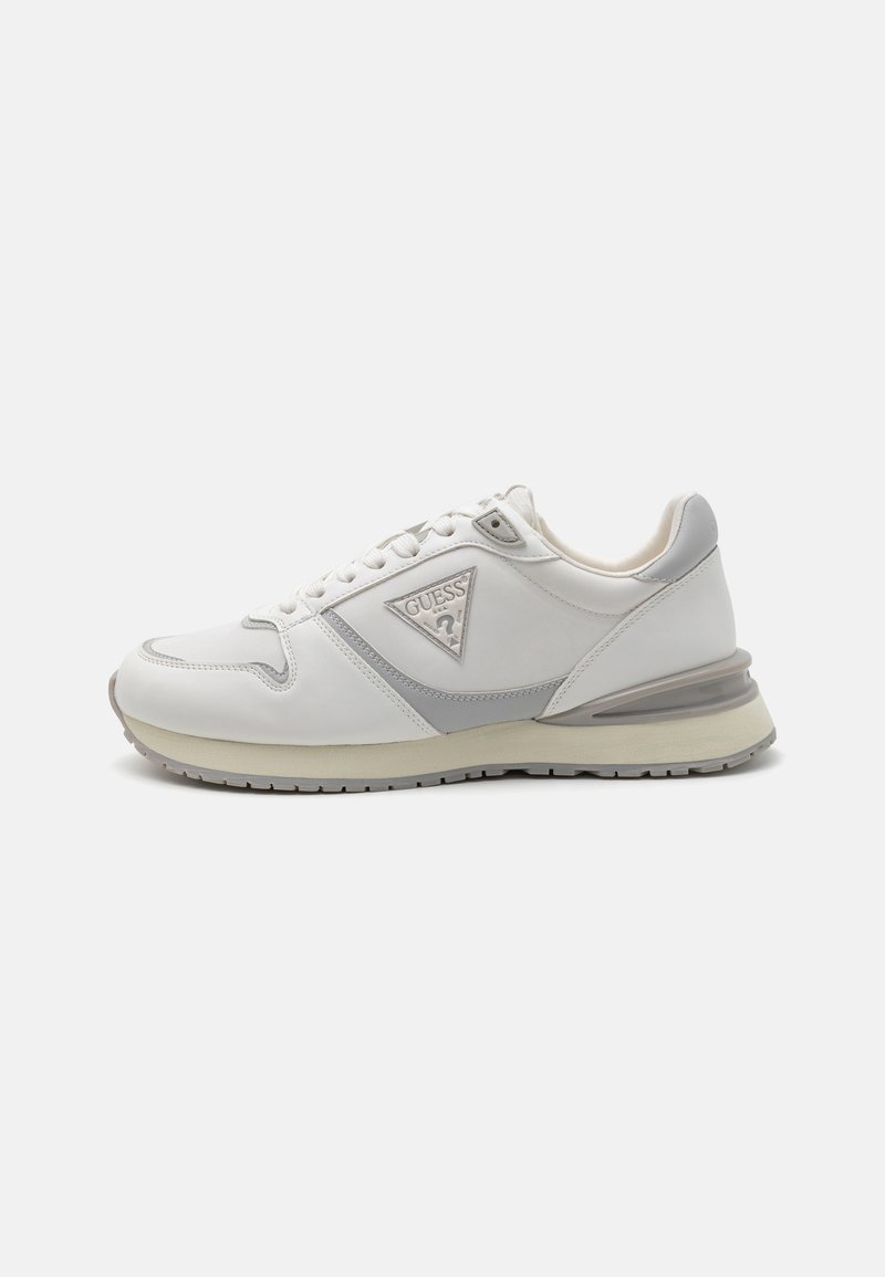 Zapatilla deportiva blanca con acentos grises, material de cuero, punta redondeada, cuello acolchado, suela de goma y un detalle de triángulo del logo en el costado.