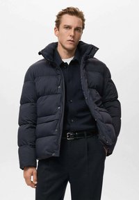 Chaqueta de plumas azul marino con segmentos acolchados, cuello alto, botones de presión y un corte relajado, fabricada con material suave y resistente al agua.