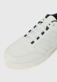 White athletic shoe featuring a smooth leather upper, mesh accents, navy laces, perforations for breathability, and a textured rubber sole.