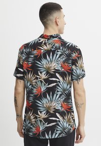 Kortermet svart skjorte med et livlig trykk av tropiske blader og blomster i blått, grønt og rødt. Glatt stoff med en avslappet passform.