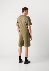Olivenfarvet kortærmet top med matchende shorts, elastisk talje og sidelomme. Glat stoftekstur, enkelt design.