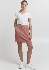 Kort rosa skjørt med snøring i livet, kombinert med en enkel hvit t-skjorte og hvite sneakers. Glatt stoff med en avslappet passform.