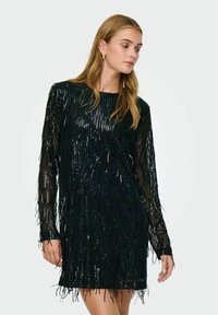 Melnā spīdīgā kleita ar garām piedurknēm, kurai visā virsmā ir frandžu detaļas. Audumam ir gluda tekstūra, radot mirdzošu efektu.
