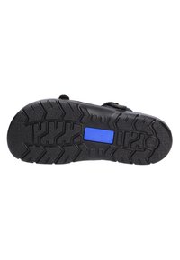 Black rubber sandal sole featuring deep tread patterns for grip, with a blue branded label. The design includes adjustable straps.