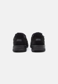 Fekete Skechers cipők, slip-on stílusú, puha béléssel, hátulról bemutatva, fehér háttéren.