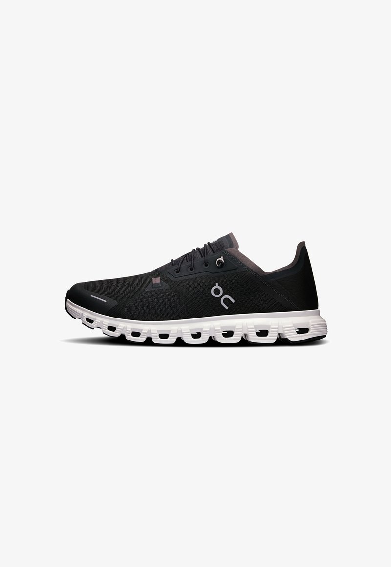 Baskets de sport noires en mesh respirant avec une surface texturée, dotées d'une semelle blanche rembourrée et d'éléments de design minimalistes.