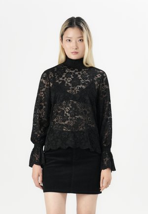 Black lace blouse with high neck, long bell sleeves, floral patterns, and scalloped hem, paired with a black skirt.