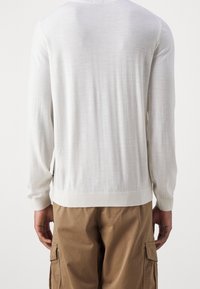 Maglione bianco leggero con maniche lunghe, scollo rotondo e orlo a coste. Indossato con pantaloni cargo color khaki, mostrano un fitting rilassato.