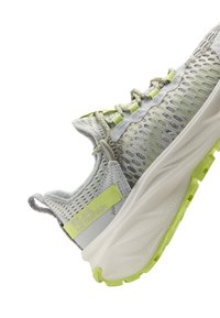 Light gray athletic shoe with mesh upper, reflective accents, and neon yellow details. Thick white midsole and grip rubber outsole.