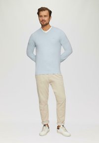Lichtblauwe, langermige trui met een V-hals, gecombineerd met beige broeken en witte sneakers. Heeft een eenvoudig ontwerp en een getailleerde uitstraling.