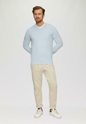 Hellblauer, langärmeliger Pullover mit V-Ausschnitt, kombiniert mit beigen Hosen und weißen Sneakers. Hat ein einfaches Design und eine taillierte Form.