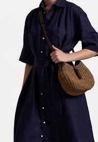 Marinblå linneklänning med korta ärmar och knytning i midjan, i kombination med en vävd stråväska med en brun läderrem.