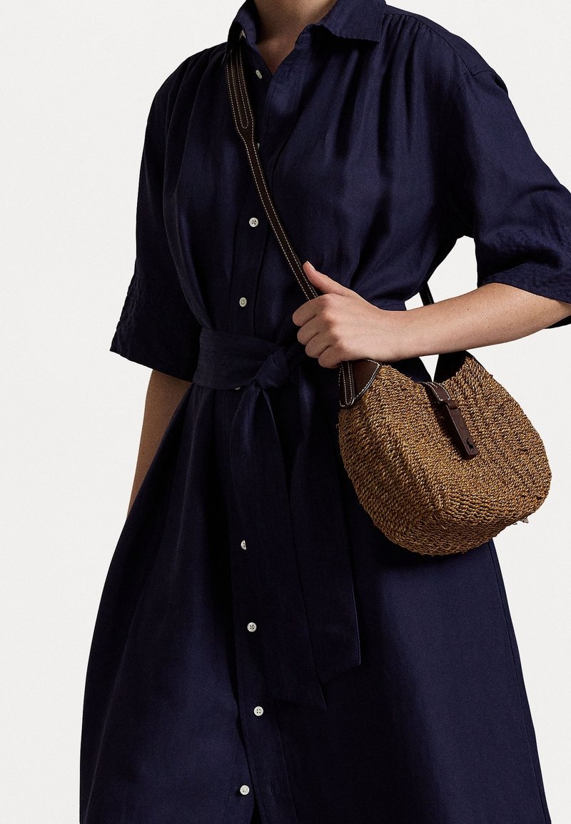 Marinblå linneklänning med korta ärmar och knytning i midjan, i kombination med en vävd stråväska med en brun läderrem.