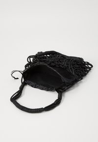 Sac tissé noir avec un design texturé, poignées en tissu et doublure intérieure lisse ; ouvert en haut avec des accents de nœud décoratifs.