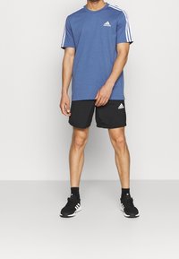 Camiseta azul de manga corta con rayas blancas en los hombros, combinada con pantalones cortos negros y zapatillas deportivas negras con detalles en blanco.