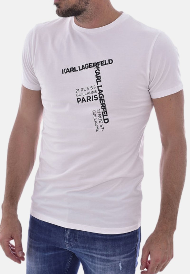 T-shirt bianco in cotone con grafiche testuali nere: "KARL LAGERFELD," "21 RUE ST-GUILLAUME," e "PARIGI." Design aderente con maniche corte.