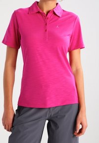 Polo rose avec une surface texturée, patte de boutonnage et petit logo sur la poitrine gauche. Associé à un pantalon gris.
