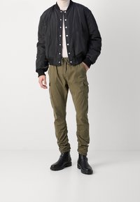 Schwarze Bomberjacke mit Druckknöpfen, olivgrüne Cargo-Hose mit elastischen Bündchen und schwarze Knöchelstiefel. Glatter Stoff und funktionale Taschen.