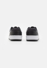 Sneakers de couro preto com sola branca. Apresentam um calcanhar texturizado e um logotipo estampado na parte de trás. Frente lisa e colarinho acolchoado.