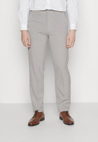 Pantalones grises claros a medida con frente plano, piernas rectas y tejido texturizado. Combinados con zapatos de vestir de cuero marrón.