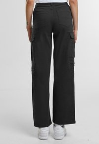 Pantaloni cargo neri con vita alta, gambe larghe e molteplici tasche sui lati. Realizzati in un resistente tessuto misto cotone.