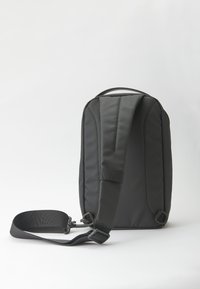 Zaino in nylon nero con tracolla regolabile, forma rettangolare, schienale imbottito e design minimalista. Presenta anelli laterali per attacchi.