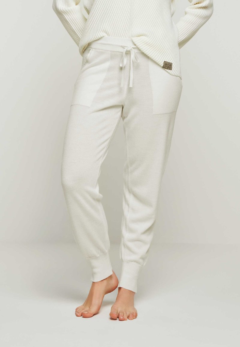 Weiße Strick-Jogginghosen mit einem Kordelzugbund, die seitliche, strukturierte Einsätze und gerippte Bündchen an den Knöcheln aufweisen. Weicher Stoffabschluss.