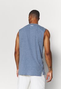 Camiseta atlética sin mangas azul con un escote redondeado, aberturas laterales y un pequeño logo en la parte trasera. Hecha de una tela ligera y con textura.