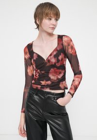Bluză cu mânecă lungă dintr-un material transparent, cu un model floral, având un decolteu adânc în V, parte frontală plisată și margine subțire din dantelă, asortată cu pantaloni din piele negri.